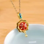 Tibetan lotus prayer wheel pendant necklace in 925 sterling silver with red agate center, displayed on wooden desktop with white porcelain bowl and engraved six-word mantra details