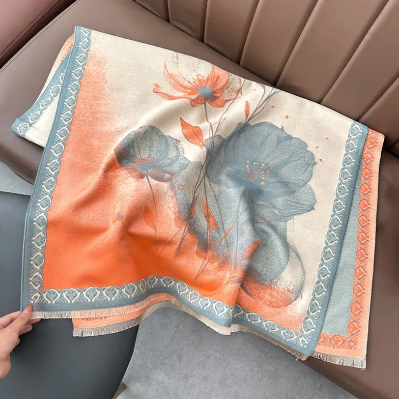 Close-up flat lay of orange-gray gradient lotus watercolor scarf on leather sofa showing woven trim detail