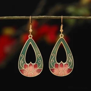 Hollow teardrop lotus enamel drop earrings in dark green and pink with gold tone trim, hung on delicate twig with red floral background