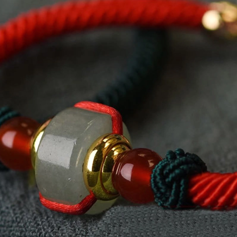 Tibetan luck bracelet macro close-up showing green aventurine barrel bead, red agate accents, and braided cord construction