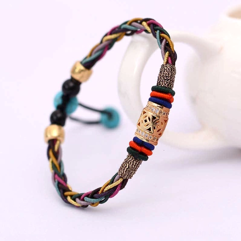Tibetan woven protection bracelet with multicolor braid, gold and turquoise beads next to white ceramic teapot, showcasing embossed charm detail