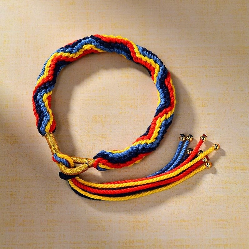 Circular braided Tibetan luck bracelet flat lay showing multi-color yarn threads and gold hardware with tassel ends on light brown background