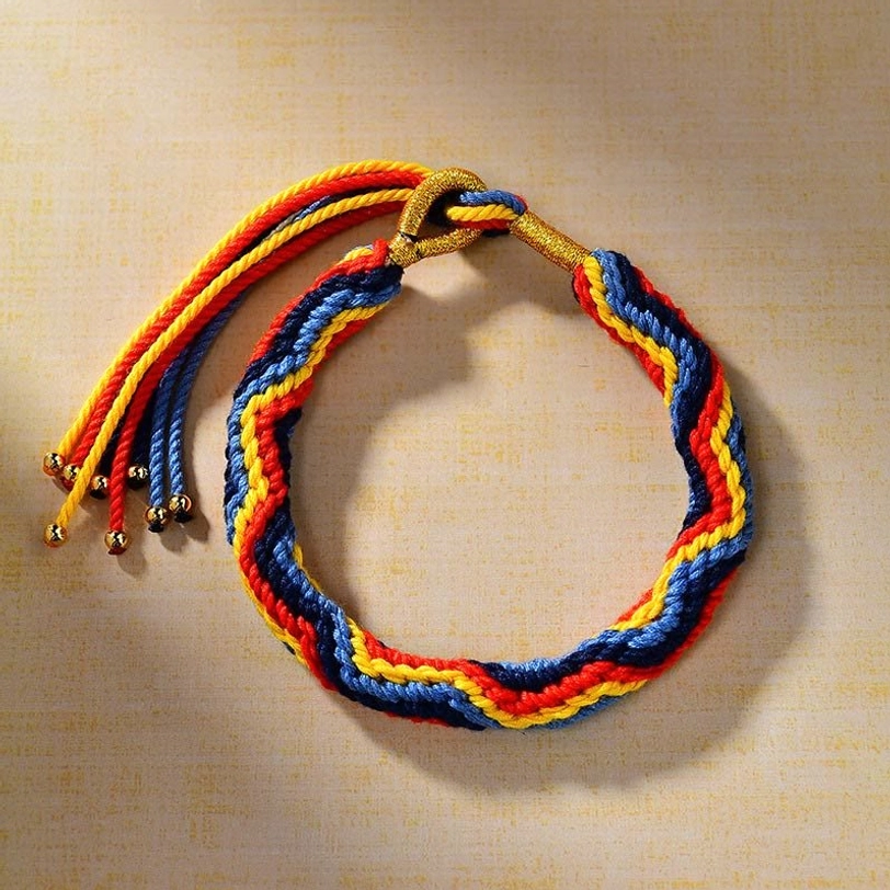 Tibetan hand-woven colorful luck bracelet with chevron braided design, multicolor woven threads and gold metal hardware displayed on light brown fabric