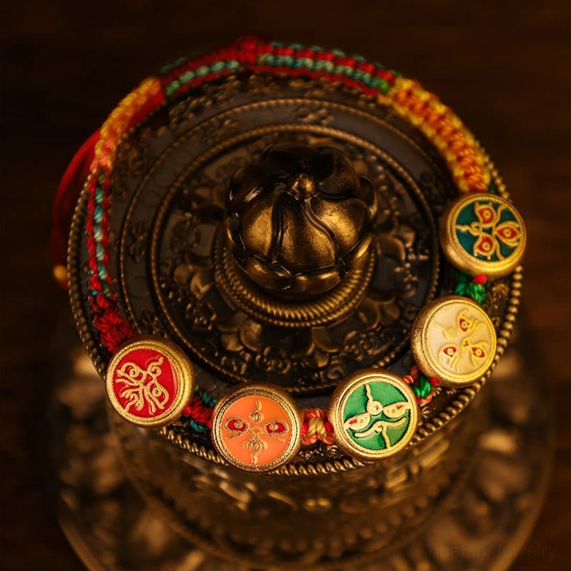 Tibetan luck bracelet arranged along vintage prayer wheel rim showing colorful braided cord and prosperity charm accents