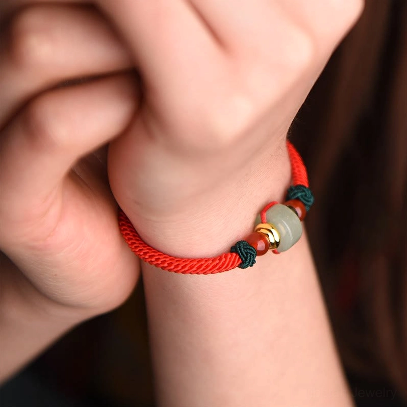 Tibetan lucky braid bracelet side view on wrist showing red woven rope with jade barrel bead and gold details