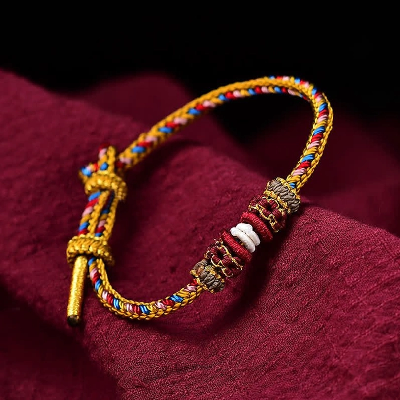 Handmade Dunhuang Tibetan lucky bracelet with multicolor braided cord and decorative knots on dark red background