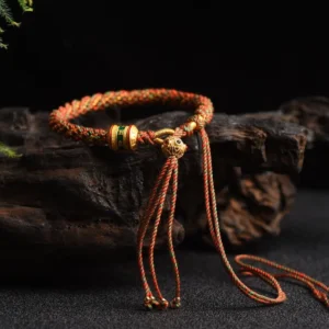 Braided Tibetan lucky string bracelet featuring gold enamel prayer wheel charm and tassel with gold end tips, flat lay side view