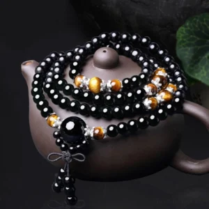 108 bead black obsidian tiger eye mala bracelet with tassel, top-down view on dark teapot background