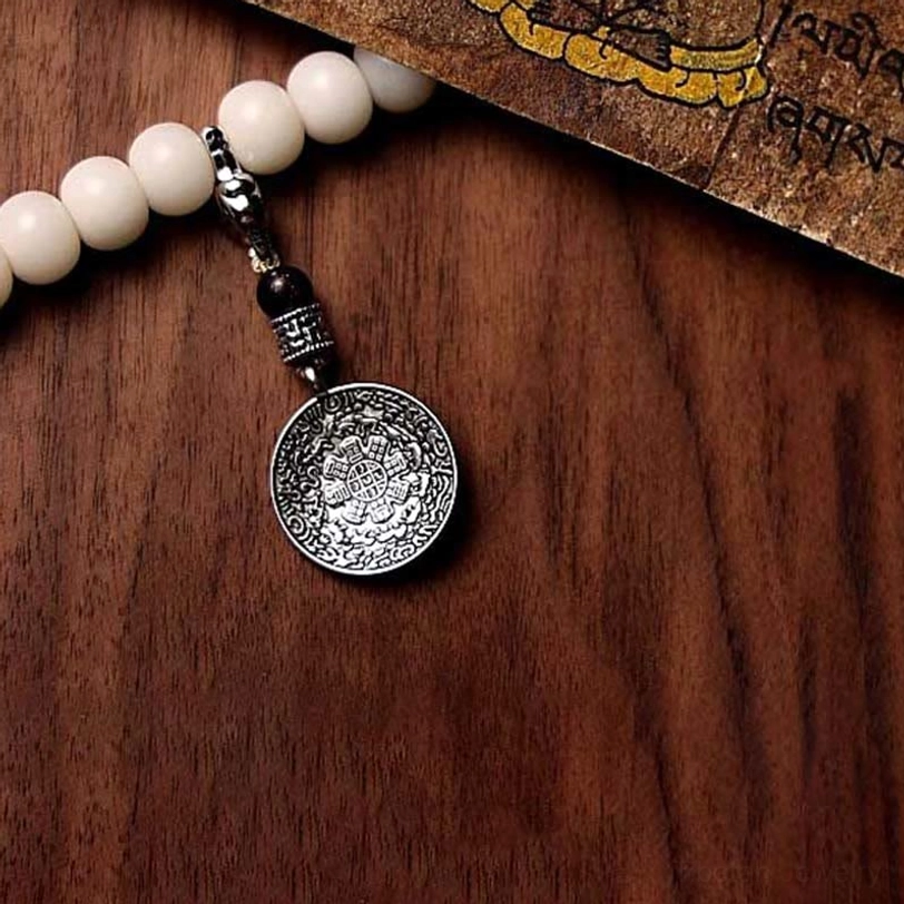 Tibetan mala beads with embossed Bagua eight trigrams silver plaque pendant and white bodhi beads on wooden table
