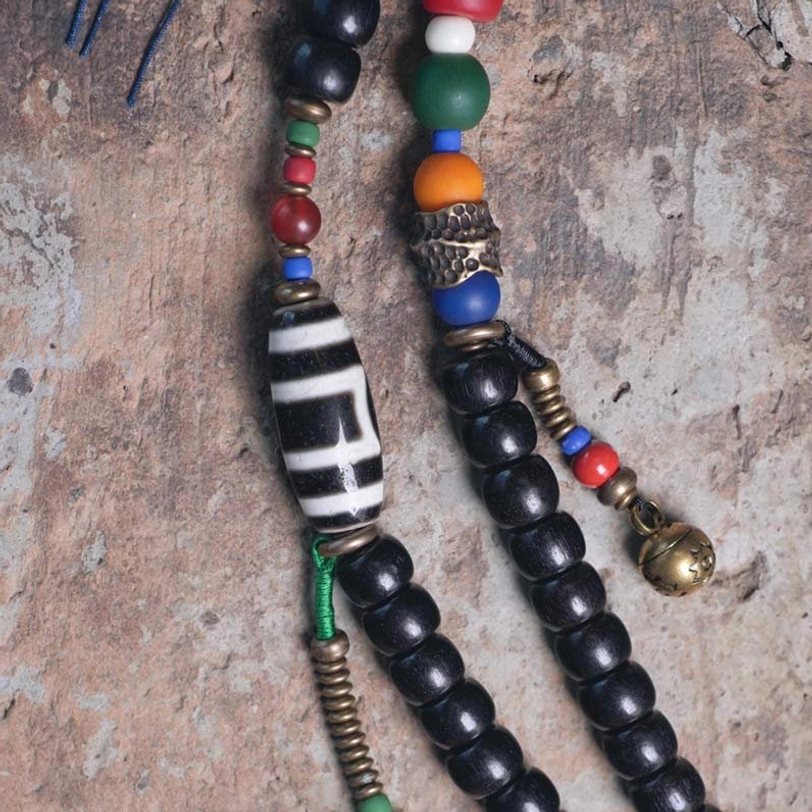 Macro close-up of Tibetan mala bead components showing dzi bead, gemstones, copper parts, brass bell charm and craftsmanship