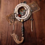 Tibetan 108 mala beads bracelet with bodhi seeds, hand-painted nine-eye dzi bead, and silver vajra pendant on wooden surface with Buddhist scriptures