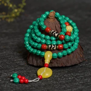 Coiled turquoise mala necklace close-up with black and white dzi beads, yellow guru bead and red tassel on dark wood display