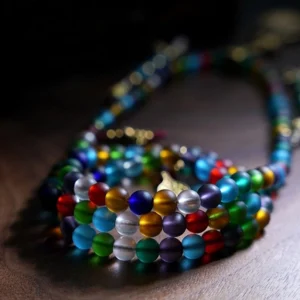 Coiled mala prayer beads showing rainbow gradient frosted glass beads with vintage metal fittings, close-up flat lay