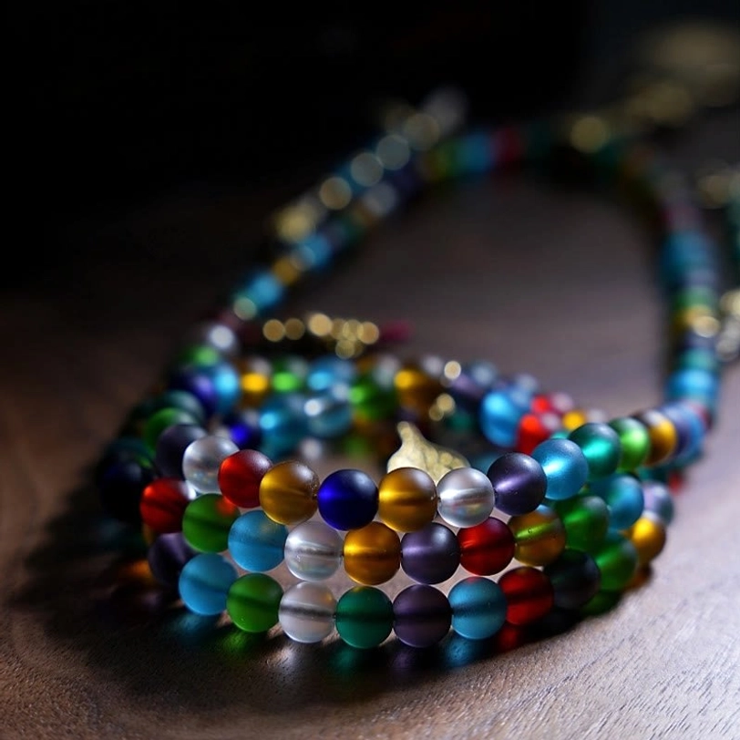 Coiled mala prayer beads showing rainbow gradient frosted glass beads with vintage metal fittings, close-up flat lay