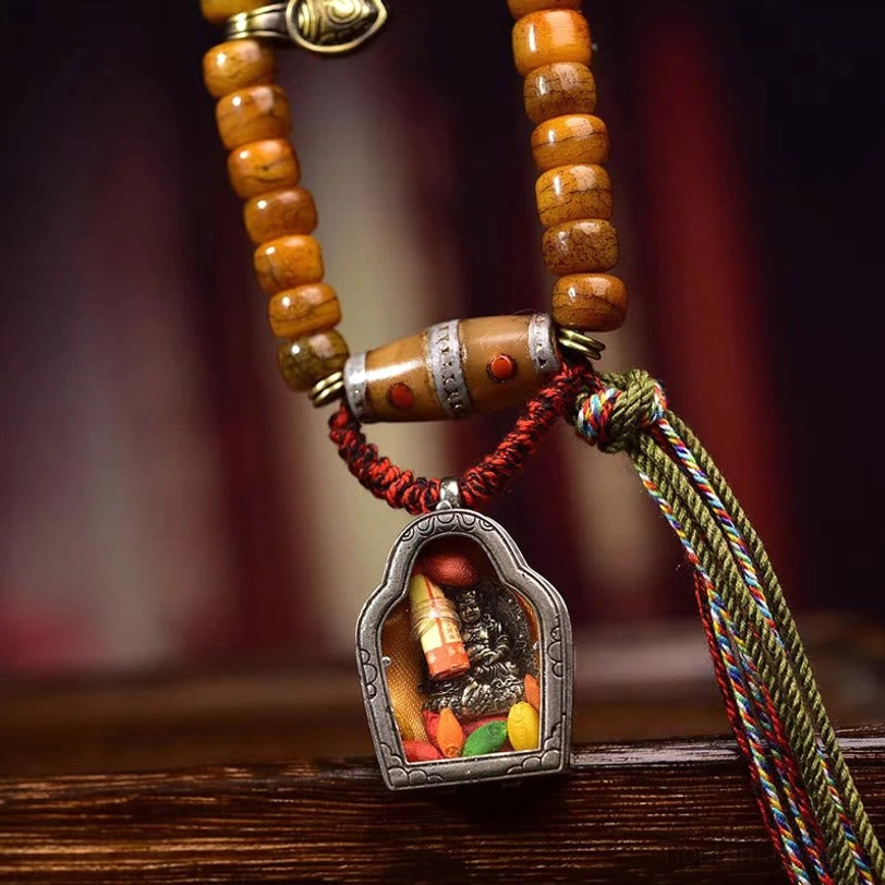 Front close-up of Tibetan mala beads with aged camel bone, Dzi bead, woven multicolor tassel, and shrine pendant