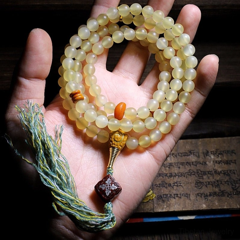 Hand holding Tibetan sheep horn mala bracelet with amber carved guru bead and green tassel detail