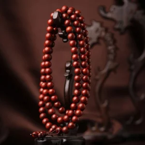 Tibetan prayer bead mala necklace hanging on vintage wooden stand, side view showing uniform reddish-brown beads with knotted tassel