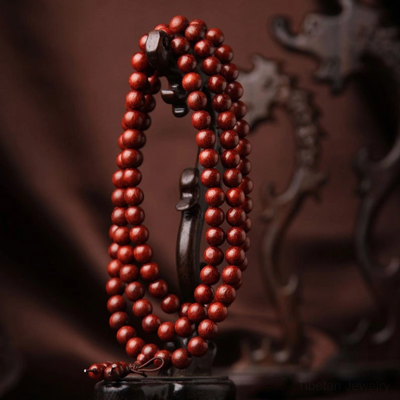 Tibetan prayer bead mala necklace hanging on vintage wooden stand, side view showing uniform reddish-brown beads with knotted tassel