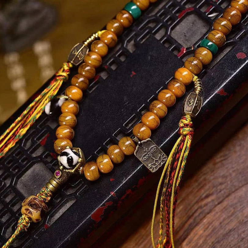 Tibetan prayer bead mala with skull guru bead and metal tag pendant on carved wooden tray - side angle