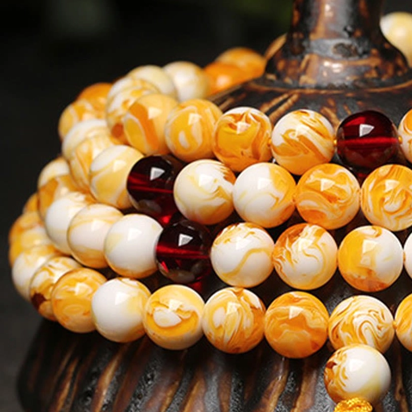 Stacked Tibetan amber malas with orange-yellow and white marbled beads, dark red spacers on carved wooden base, top-down view