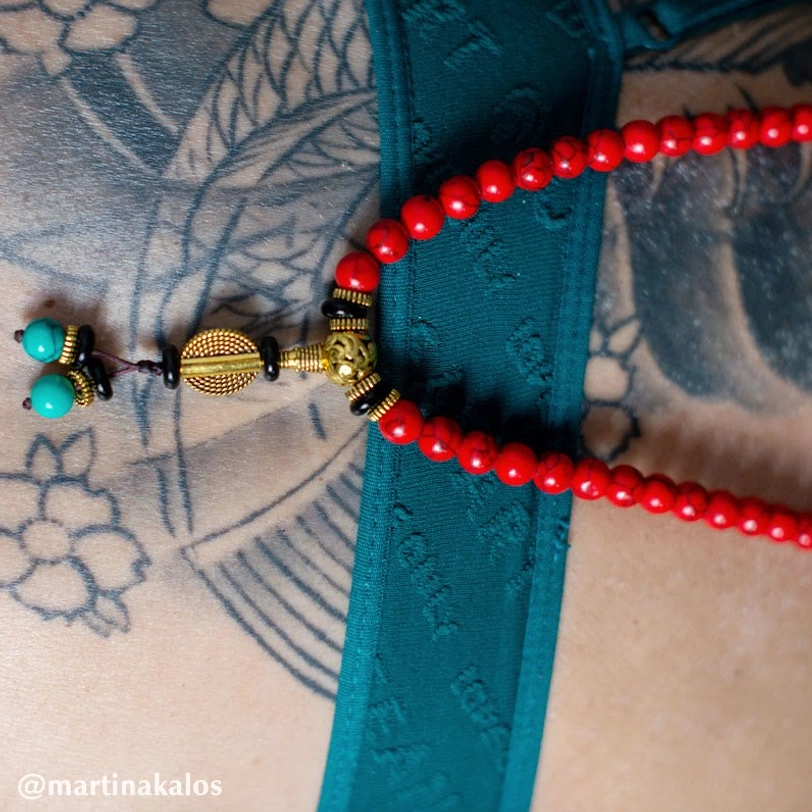 Flat lay close-up of Tibetan mala bead strands with red beads turquoise spacers and tassel pendant on dark surface