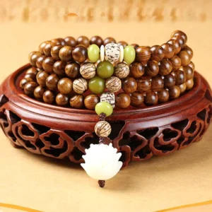 Top-down view of 108-bead rosewood prayer mala with lotus charm and green spacer beads on carved wooden display base