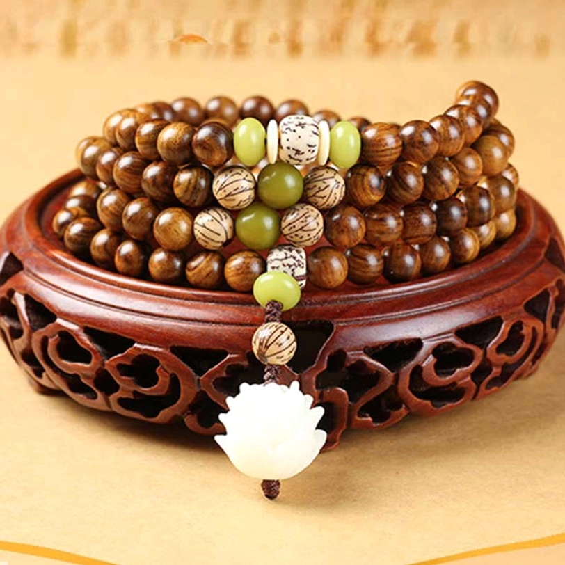Top-down view of 108-bead rosewood prayer mala with lotus charm and green spacer beads on carved wooden display base
