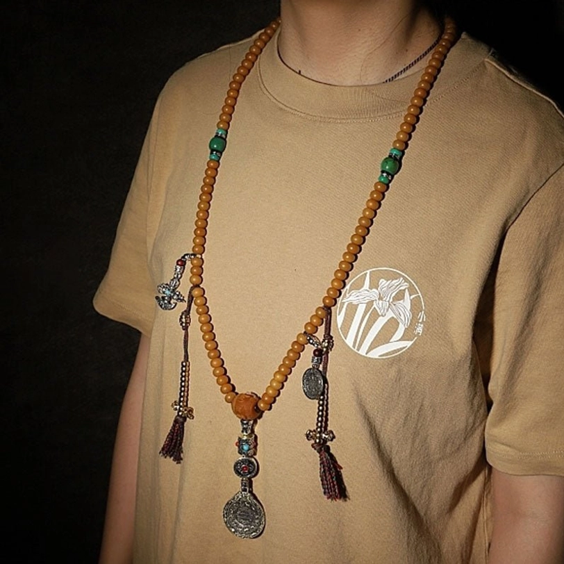 Tibetan mala bracelet flat lay with hand model and Buddhist religious accessories including wrap-around tan beads, silver charms, and extra figurine decor