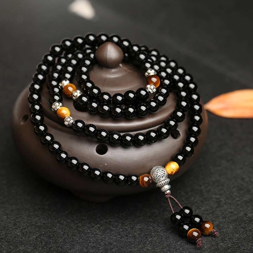 Multi-layer tibetan mala bracelet close-up showing black obsidian and brown tiger eye beads with silver hardware and hanging tassel