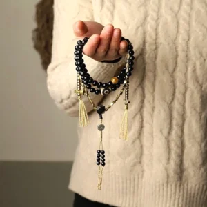 Person wearing black onyx mala bead bracelet with brass tassel accents close-up detail shot
