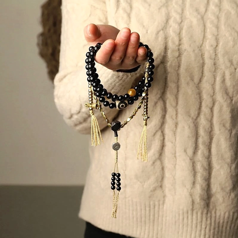 Person wearing black onyx mala bead bracelet with brass tassel accents close-up detail shot