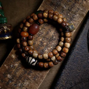 Triple wrap Tibetan mala bracelet featuring brown bodhi seeds, red agate beads, and sacred dzi ornament on aged Buddhist scripture paper
