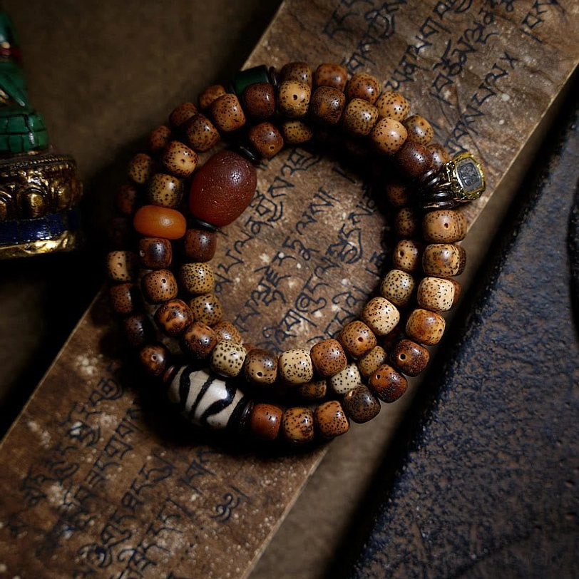 Triple wrap Tibetan mala bracelet featuring brown bodhi seeds, red agate beads, and sacred dzi ornament on aged Buddhist scripture paper