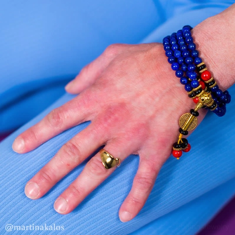 Hand wearing lapis lazuli mala bracelet multi-strand with red and brass accents paired with gold ring