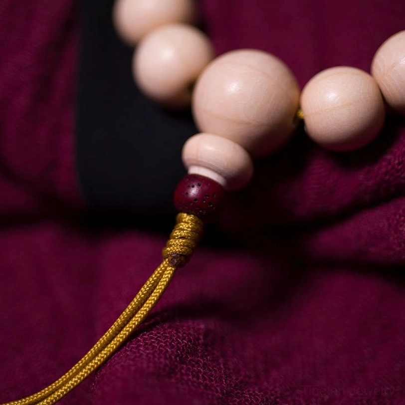 Close-up detail of Abelia Biflora mala bracelet tail showing red accent bead, smooth wooden beads texture, and hand-woven yellow tassel with counter beads