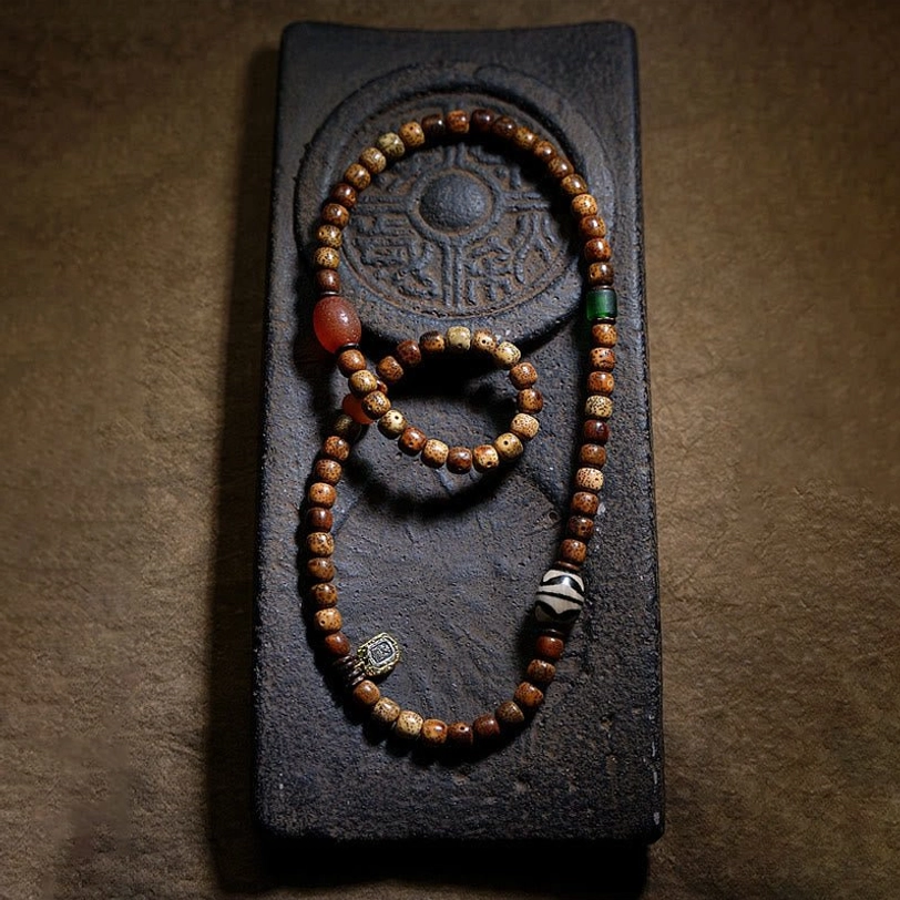 Three sizes of Tibetan mala bracelets displayed on carved dark stone tray showing assorted agate beads and dzi bead decorations
