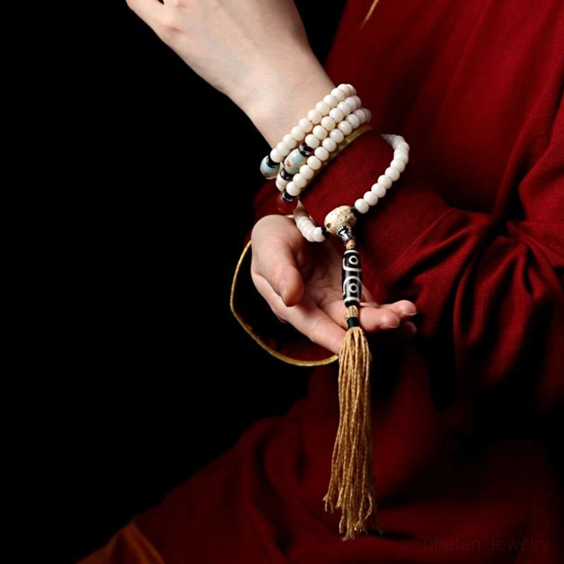 Hand holding stacked tibetan mala bracelets with bodhi beads and dzi bead against traditional red clothing
