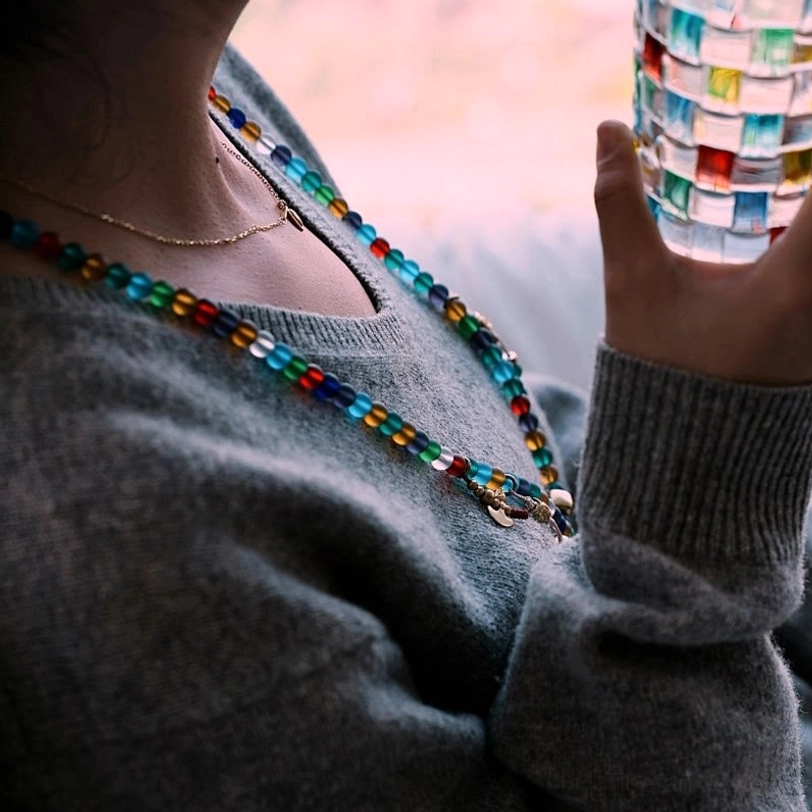Woman wearing wearable Tibetan mala bead necklace with multicolored glass beads around neck, lifestyle indoor shot