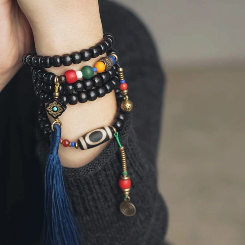 Stacked Tibetan mala bead bracelets on wrist showing dzi bead, copper charm and blue tassel multi-wrap style