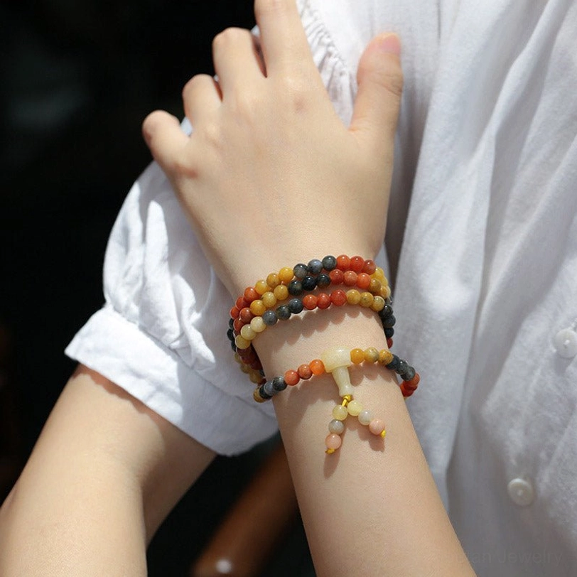 Stacked natural agate mala bracelets worn on human wrists with white shirt, close-up wrist view featuring mixed-color beads including red agate and black onyx with decorative tassels