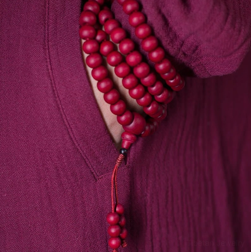 Tibetan mala bracelet wrapped around wrist showing how prayer beads sit on skin with hanging tassel against traditional maroon robe collar