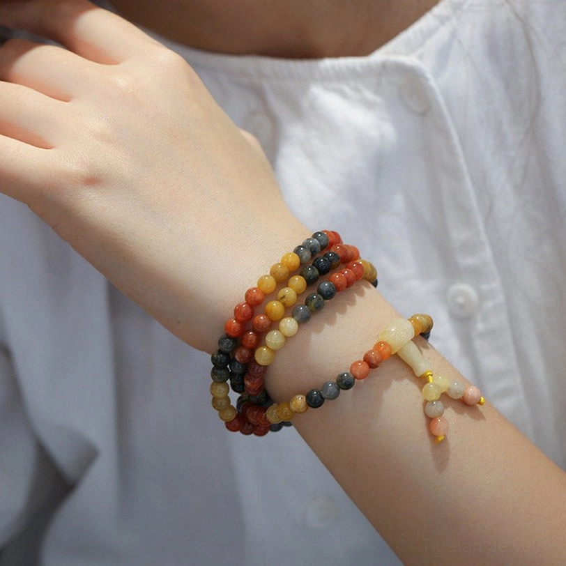 Two natural agate 108-bead mala bracelets worn on human wrist with white shirt, side close-up view featuring different color tones of red agate and yellow agate stones with decorative tassels