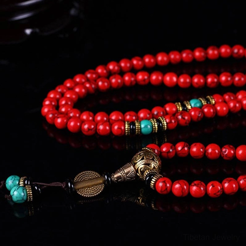 Extreme close-up of Tibetan mala hardware showing ornate bronze metalwork with turquoise beads and red bead details