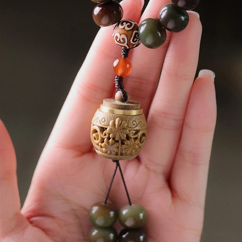 Close-up of Tibetan mala bead bracelet components including carved Dzi bead, agate spacer, and prayer box pendant