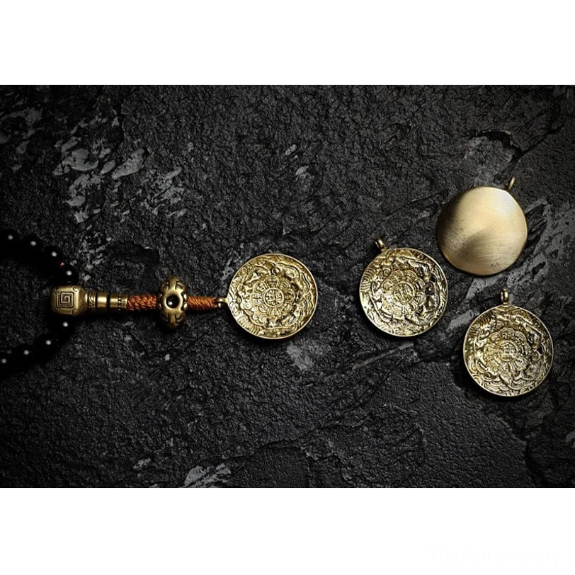 Mala pendant accessory set featuring multiple embossed protective amulets in brass with black onyx and tiger eye beads on cracked stone texture