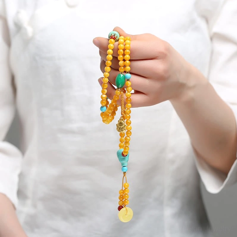 Hand holding Tibetan amber mala with long tassel and gemstone decorations showing length and craftsmanship details