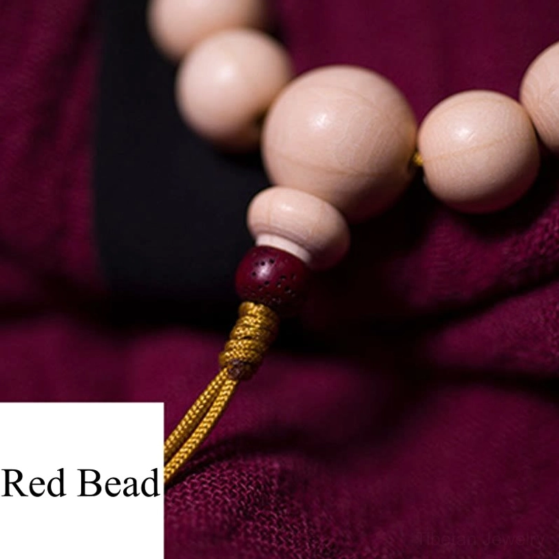 Close-up of mala bracelet tail knot showing red accent bead, hand-woven yellow thread tassel, and detail of bead assembly on dark cloth background
