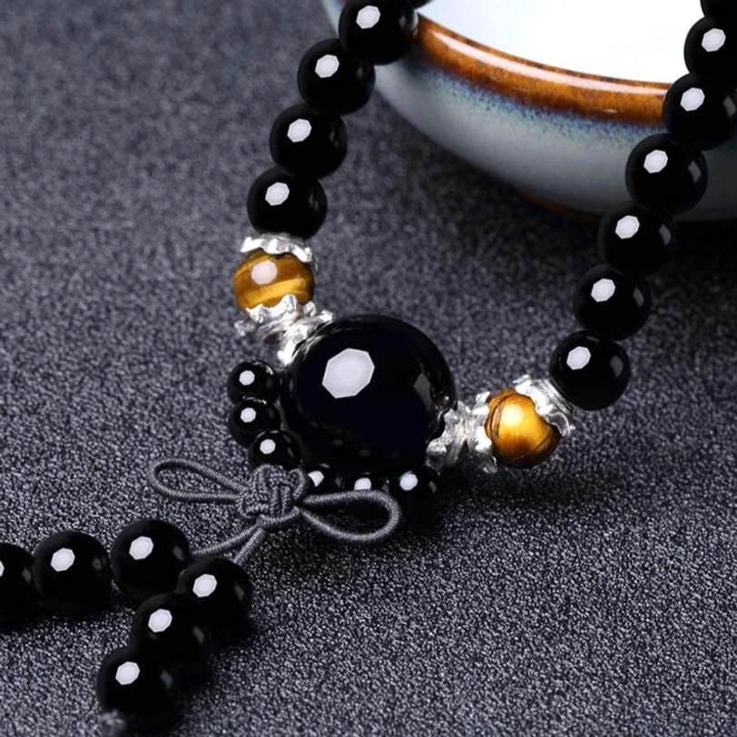 Detail view of tibetan mala tassel and mixed obsidian agate bead design on dark ceramic background