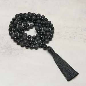 Overhead view of 108-bead black onyx and lava rock tibetan mala necklace with long silk tassel on neutral background