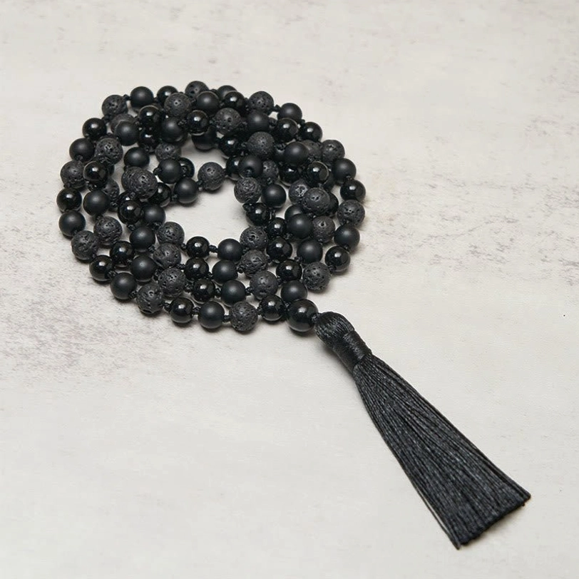 Overhead view of 108-bead black onyx and lava rock tibetan mala necklace with long silk tassel on neutral background